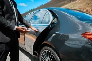 a chauffeur open door for a business man who book a private car service in a sunny day